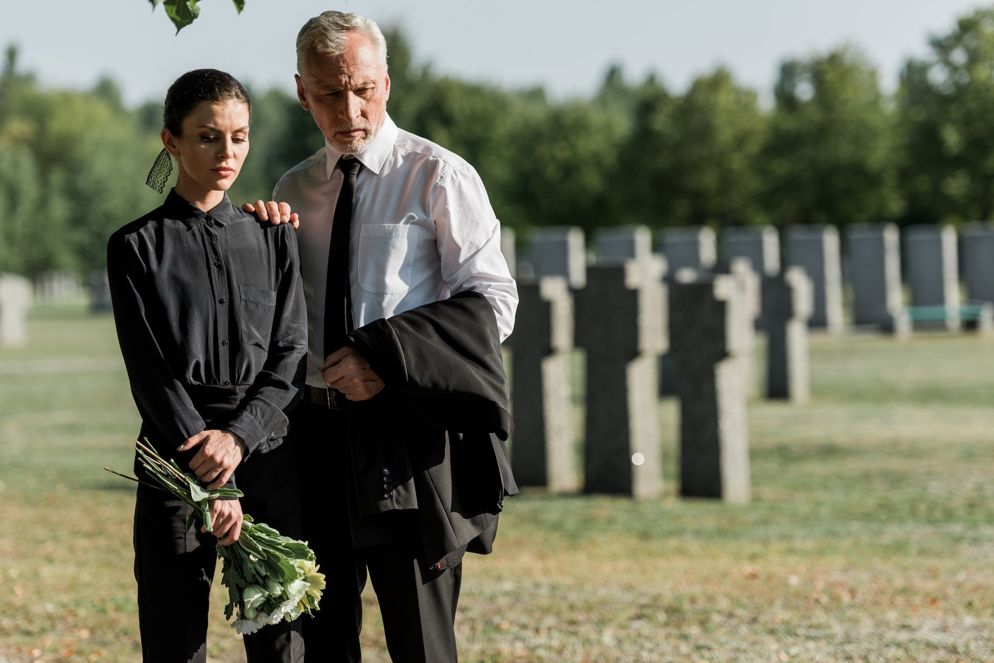 senior man standing with attractive woman holding flowers on funeral